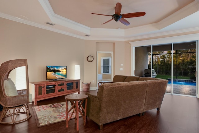 living room with dark wood-type flooring, a tray ceiling, and ornamental molding