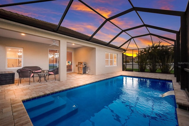 pool at dusk with glass enclosure, a grill, ceiling fan, and a patio