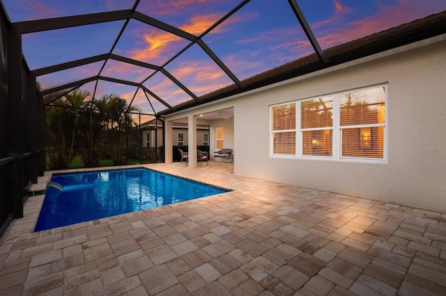 pool at dusk with ceiling fan, a lanai, pool water feature, and a patio