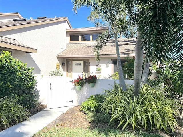 view of front facade with a fenced front yard, stucco siding, a shingled roof, and a gate