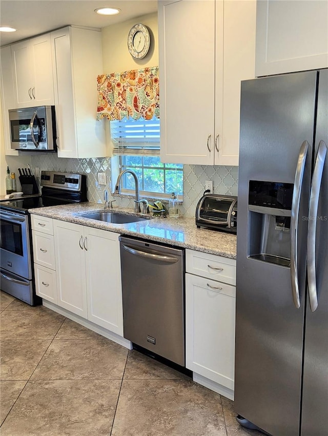 kitchen featuring appliances with stainless steel finishes, sink, backsplash, white cabinets, and light stone counters