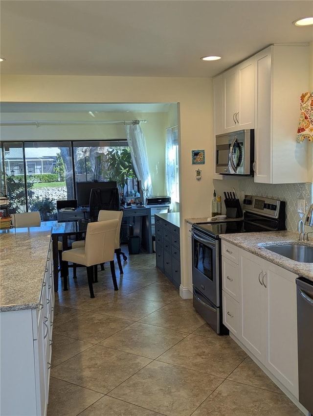 kitchen with sink, appliances with stainless steel finishes, white cabinets, light stone countertops, and backsplash