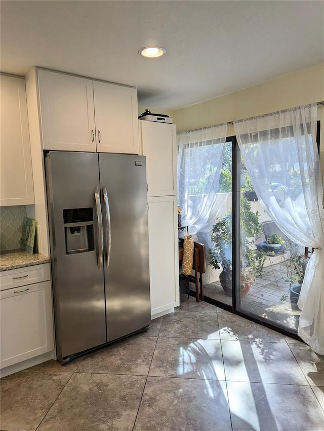 kitchen with white cabinetry, backsplash, light stone counters, and stainless steel fridge with ice dispenser