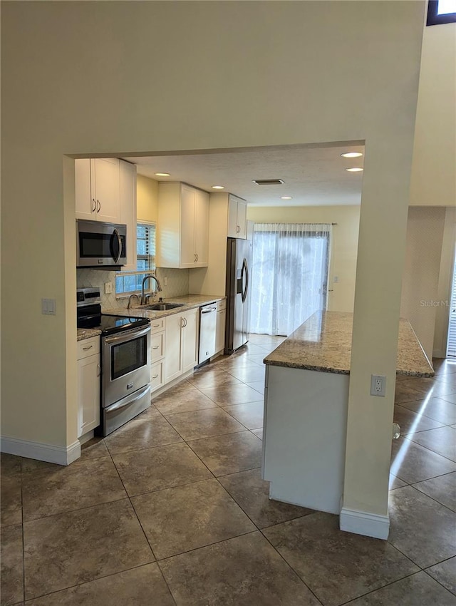 kitchen with appliances with stainless steel finishes, sink, white cabinets, decorative backsplash, and light stone countertops