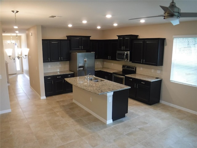 kitchen with sink, appliances with stainless steel finishes, light stone countertops, a kitchen island with sink, and backsplash