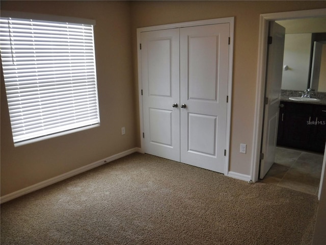 unfurnished bedroom featuring a closet, connected bathroom, sink, and carpet