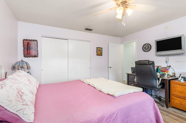 bedroom featuring ceiling fan, a closet, light hardwood / wood-style floors, and a textured ceiling