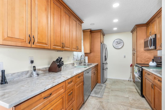 kitchen featuring sink, light stone countertops, a textured ceiling, and appliances with stainless steel finishes