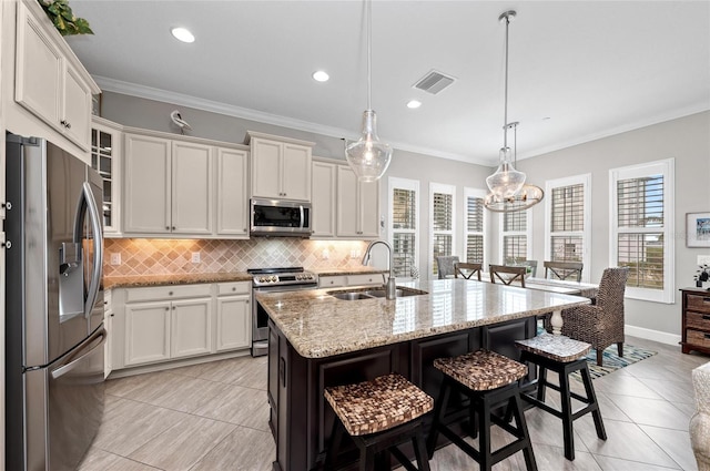 kitchen with sink, hanging light fixtures, stainless steel appliances, white cabinets, and a center island with sink