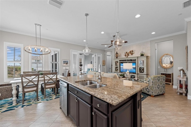 kitchen featuring decorative light fixtures, crown molding, light stone countertops, dark brown cabinets, and a center island with sink