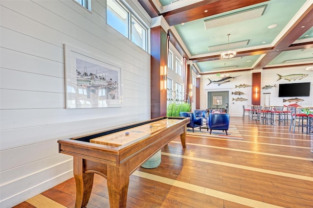 recreation room featuring wooden walls, a tray ceiling, hardwood / wood-style floors, and a towering ceiling