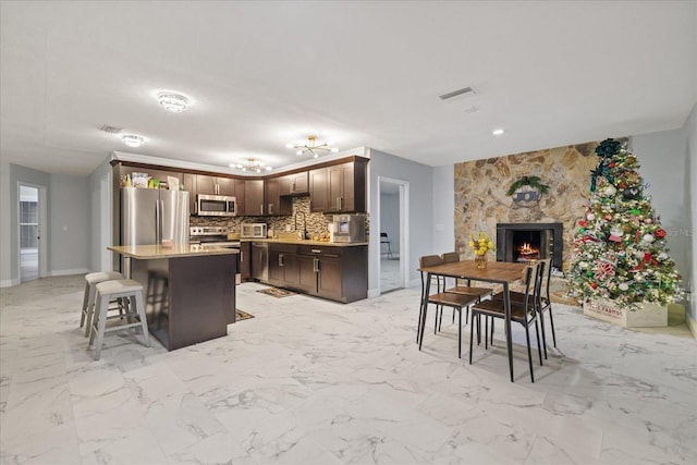 kitchen featuring appliances with stainless steel finishes, tasteful backsplash, a kitchen bar, a center island, and dark brown cabinets