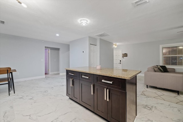 kitchen featuring a center island, dark brown cabinets, and light stone counters