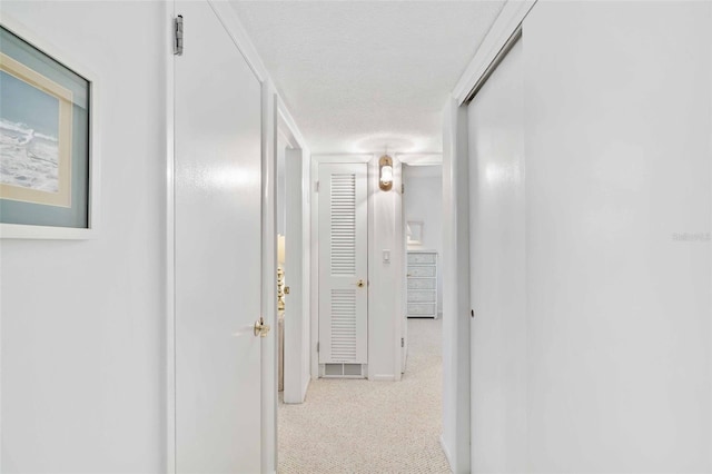 hall with light colored carpet and a textured ceiling