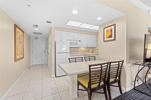 kitchen featuring light tile patterned floors, white appliances, a breakfast bar, a skylight, and white cabinets