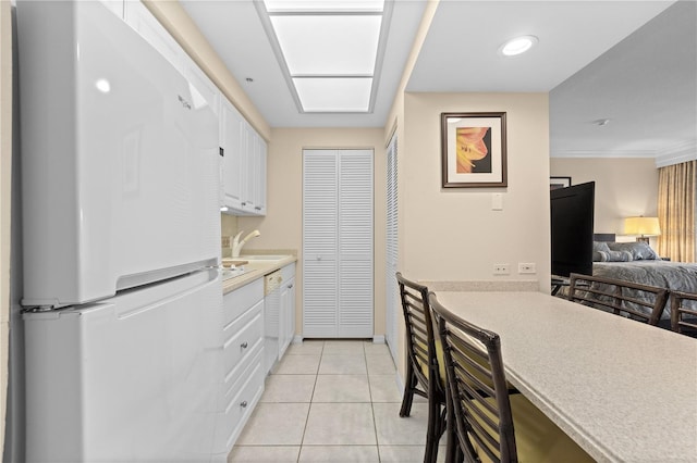 kitchen featuring white refrigerator, white cabinetry, and light tile patterned flooring