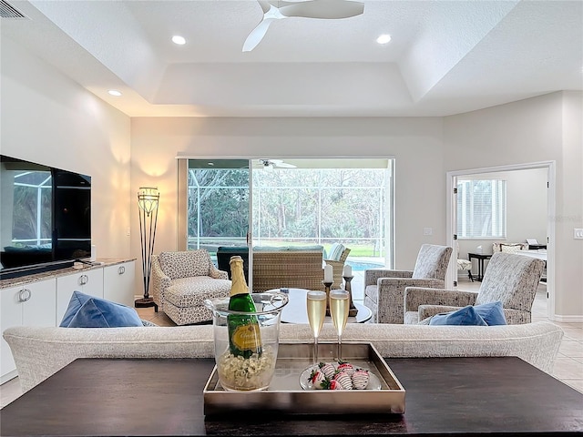 tiled living room with ceiling fan and a tray ceiling