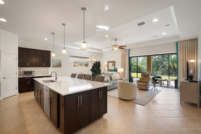 kitchen featuring sink, hanging light fixtures, a center island with sink, stainless steel dishwasher, and a raised ceiling