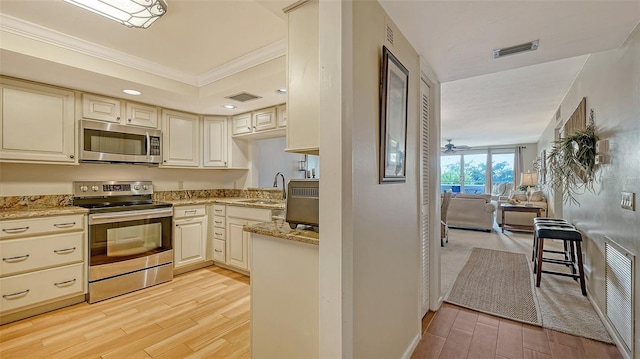 kitchen featuring appliances with stainless steel finishes, cream cabinets, ornamental molding, light stone countertops, and light hardwood / wood-style flooring