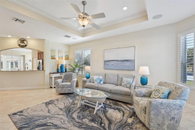 tiled living room featuring a tray ceiling, plenty of natural light, ornamental molding, and ceiling fan with notable chandelier