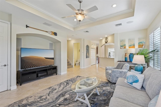 living room with light tile patterned flooring, ceiling fan, ornamental molding, and a tray ceiling