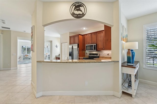 kitchen with light tile patterned floors, appliances with stainless steel finishes, tasteful backsplash, light stone countertops, and kitchen peninsula