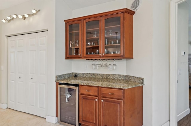 bar with light tile patterned floors, beverage cooler, and light stone counters