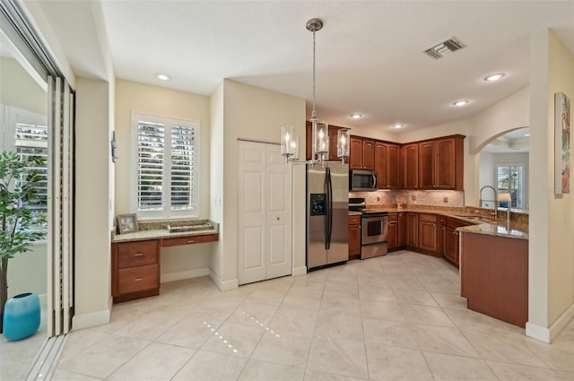 kitchen with sink, built in desk, hanging light fixtures, stone counters, and stainless steel appliances