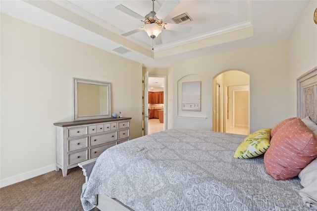 bedroom with ensuite bath, ceiling fan, carpet flooring, ornamental molding, and a raised ceiling