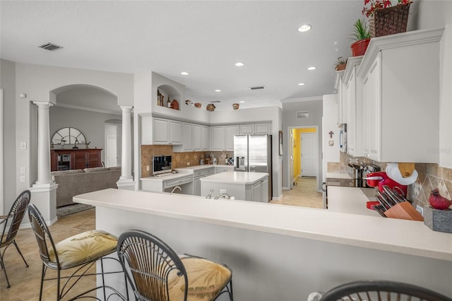 kitchen with a breakfast bar area, stainless steel fridge, ornamental molding, kitchen peninsula, and ornate columns