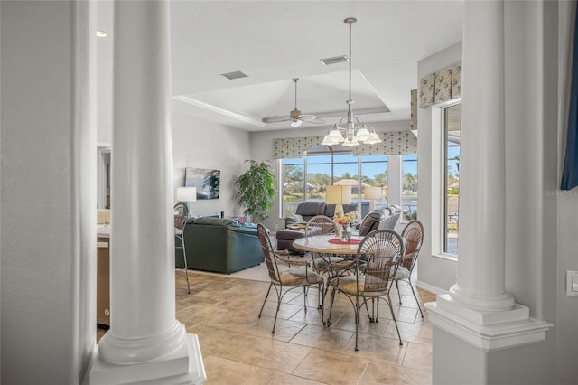 dining space with a raised ceiling, light tile patterned flooring, ceiling fan with notable chandelier, and ornate columns