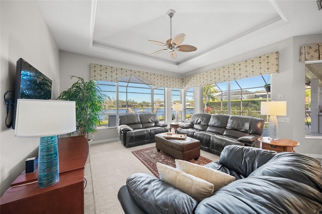 living room with ceiling fan, plenty of natural light, and a tray ceiling