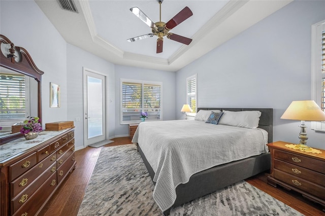 bedroom featuring a raised ceiling, ornamental molding, dark wood-type flooring, and access to exterior