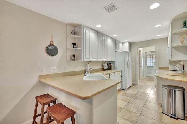 kitchen featuring sink, white appliances, white cabinets, a kitchen bar, and kitchen peninsula