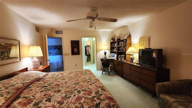 carpeted bedroom with a textured ceiling, a walk in closet, and ceiling fan