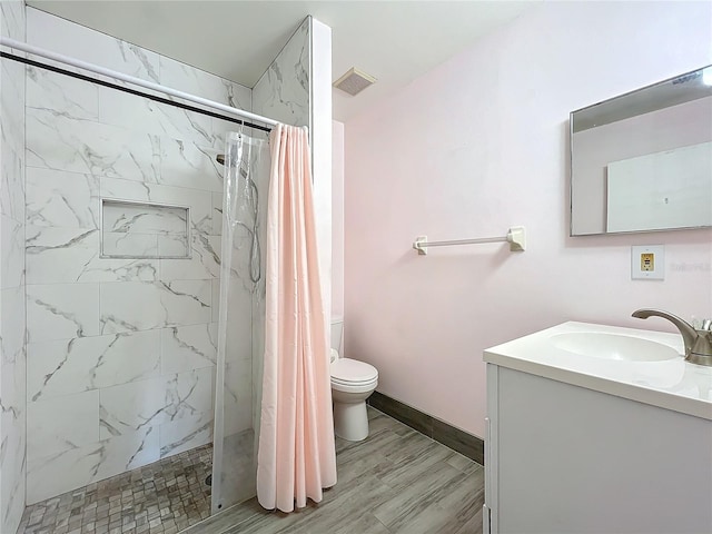 bathroom featuring vanity, wood-type flooring, tiled shower, and toilet