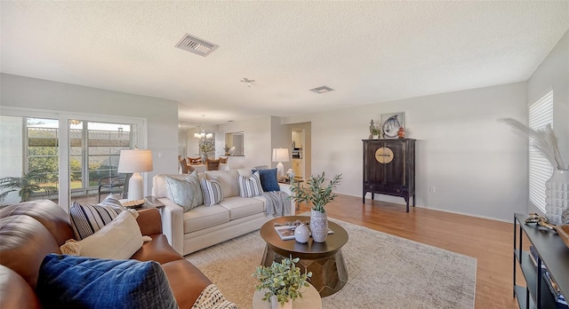 living room with light hardwood / wood-style floors, a textured ceiling, and a notable chandelier