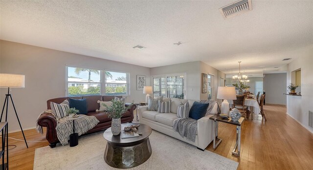 living room with an inviting chandelier, light hardwood / wood-style floors, and a textured ceiling