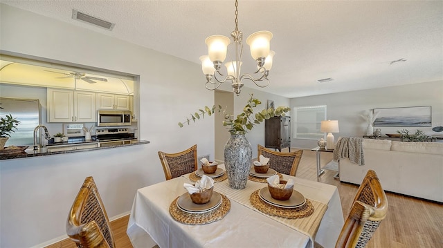 dining room with ceiling fan with notable chandelier, sink, light hardwood / wood-style floors, and a textured ceiling