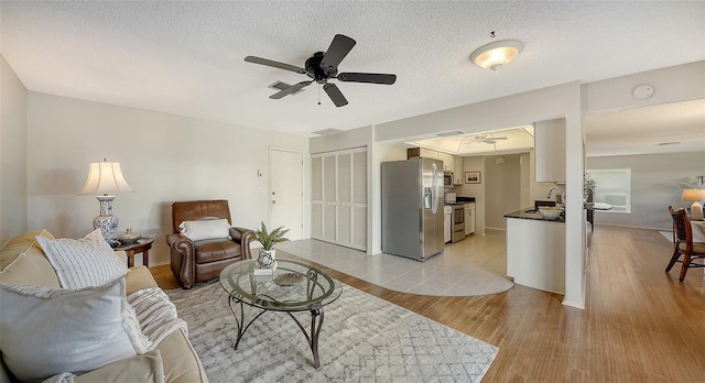 living room featuring sink, light hardwood / wood-style flooring, a textured ceiling, and ceiling fan