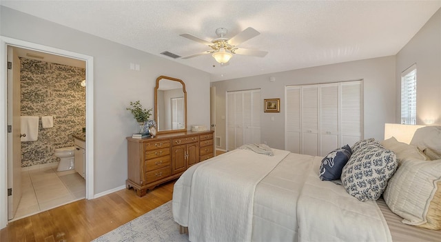 bedroom featuring ensuite bathroom, two closets, ceiling fan, light hardwood / wood-style floors, and a textured ceiling