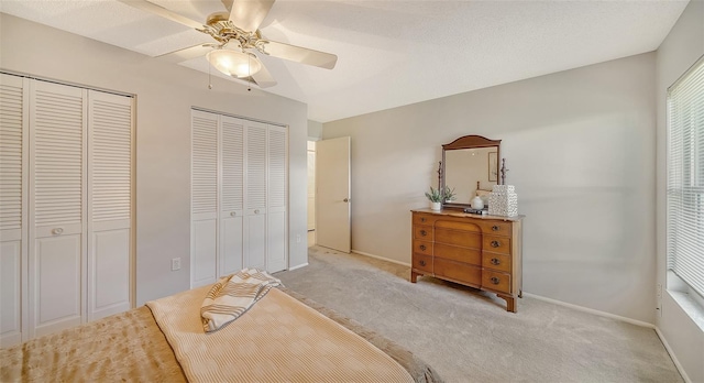 bedroom with two closets, light colored carpet, ceiling fan, and a textured ceiling