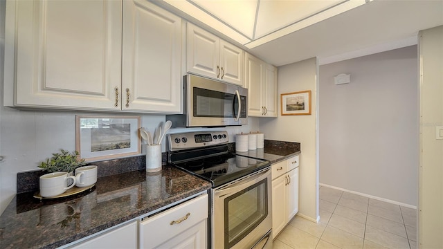 kitchen with white cabinetry, appliances with stainless steel finishes, light tile patterned floors, and dark stone countertops