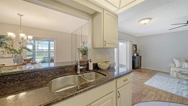 kitchen with hanging light fixtures, sink, ceiling fan with notable chandelier, and dark stone counters