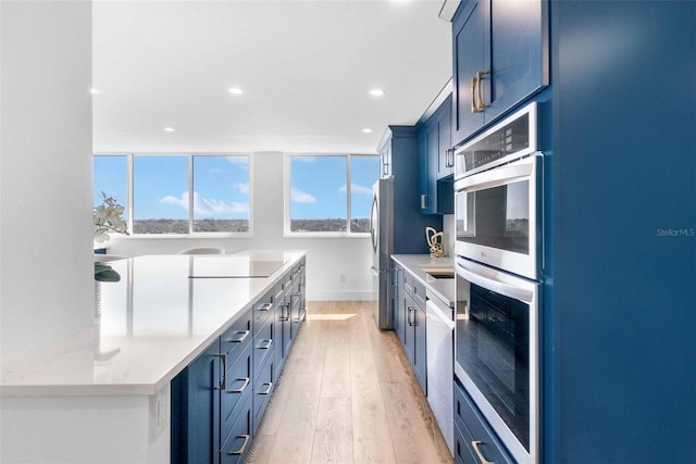 kitchen with blue cabinetry, light hardwood / wood-style floors, and appliances with stainless steel finishes