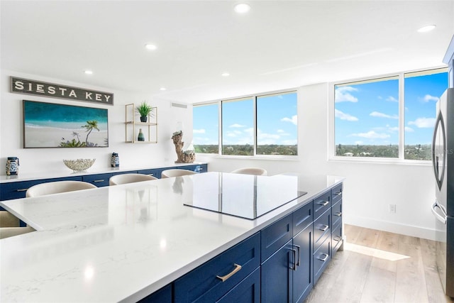 kitchen with blue cabinets, stovetop, a wealth of natural light, and light stone counters