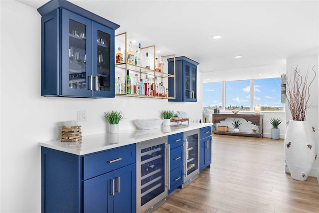 bar featuring hardwood / wood-style flooring, blue cabinetry, and beverage cooler