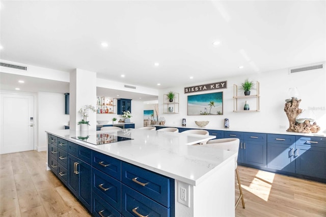 kitchen featuring a kitchen island, blue cabinets, a breakfast bar area, black electric stovetop, and light wood-type flooring