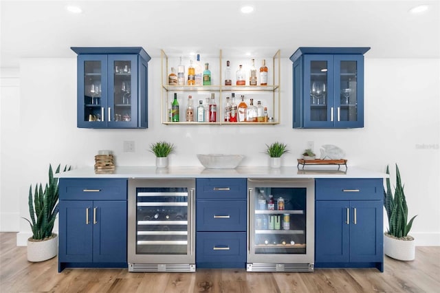 bar with wine cooler, light hardwood / wood-style floors, and blue cabinets