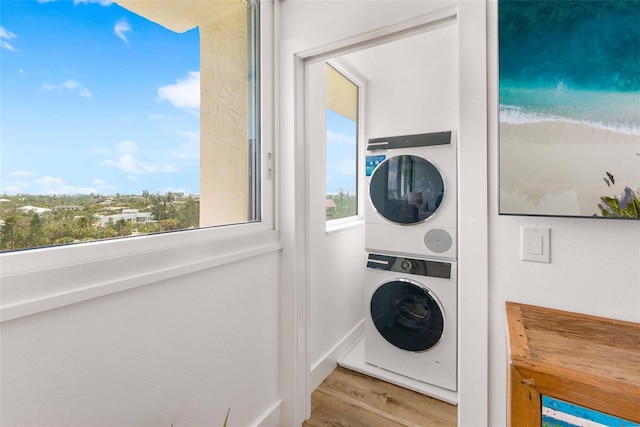 washroom with a water view, stacked washer and dryer, a beach view, and light hardwood / wood-style flooring